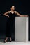 Woman poses in black dress and high heel shoes near lectern