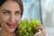 Woman posing with a bunch of grapes and smiling.