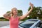 Woman posing at convertible car and taking selfie