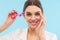 Woman posing over blue background holding lash curler doing makeup