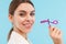 Woman posing over blue background holding lash curler doing makeup