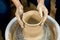 The woman potters hands formed by a clay pot on a potters wheel. The potter works in a workshop