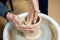 The woman potters hands formed by a clay pot on a potters wheel. The potter works in a workshop