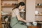 Woman pottery maker works in clay studio on pottery wheel against shelves with vases and pots.