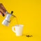 Woman poured Moka coffee into the white cup with roasted, coffee beans on a yellow paper background. Copy space for your text