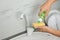 Woman pouring cleaning product for dish washing onto sponge near kitchen sink