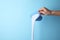 Woman pouring laundry detergent from measuring container against blue background, closeup