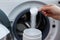 Woman pouring laundry detergent from measuring container against white background, closeup. Woman throws laundry