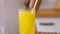 Woman pouring orange lemonade into glass. Close up of filling transparent glass with soda in kitchen.