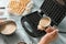 Woman pouring raw dough in modern waffle maker on light table