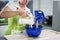 A woman is pouring some powder into a bowl of dough and uses a s