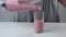 Woman is pouring strawberry smoothies in glass from blender cup, closeup view.