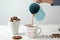 Woman pouring tasty cocoa from jug into cup on white table