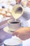 Woman Pours Milk Into a Cup of Coffee Holding a Mug and a Saucer over the Table. Coffee Catering Services at a Hotel, Event,