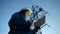 A woman power engineer in white helmet inspects power line using data from electrical sensors on a tablet. High voltage