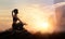 Woman practices meditating yoga at is an asana on a stone, sunset