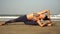 A woman practices yoga on a beautiful sandy beach. Flexible woman is training at sea.