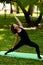 Woman practices yoga in morning in park in fresh air. Exalted Crescent Lunge pose