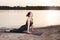 A woman practices yoga on the river bank at the beach at sunset. Cobra pose, upward facing dog asana.