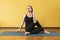 A woman practicing yoga, doing the Ardha Matsyendrasana exercise, half-king of fish pose, sits on a mat in the studio