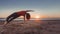 woman practicing yoga exercises while sun peeks over horizon of beach