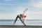 woman practicing yoga in Extended Triangle Pose with ocean and blue sky on background