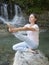 Woman is practicing yoga in Heron Pose Krounchasana pose at mountain lake waterfall, girl meditation outdoors