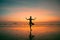 An woman practicing yoga on the ocean side, the silhouette of awesome sunset.