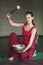 A woman practicing yoga, performing sound meditation with a metal bowl, sits on a mat in the studio