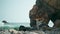 Woman practicing yoga standing one leg on rocky Ursa seashore summer day.