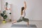 Woman practise yoga performs. Pose on mat inside of cozy room with plants and greenery. Healthy lifestyle concept.