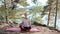 Woman practises yoga at sunrise in pine forest. Silhouette of young spiritual girl meditates in lotus pose nature