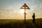 woman prays in front of a Christian cross at sunset.