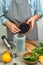 Woman prepares a healthy detox drink in a blender - a green smoothie with fresh fruits, berries, green spinach and avocado