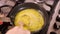 Woman prepares and mixes scrambled eggs in pan on gas stove in home kitchen