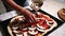 A woman prepares pizza at home, puts slices of champignons on a rolled out dough with tomato sauce and black olives