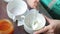 Woman preparing cream for making cakes. Mixes cream cheese and food coloring. Nearby is a jar of jam.