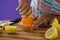 Woman preparing lemon juice from juicer against violet background