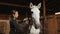 Woman preparing white horse for dressage training, cleaning stallion with brush