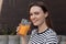 Woman with pretty smile holding in hand glass of refreshing orange drink, portrait closeup. Attractive girl drink tasty