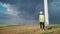 Woman Professional Ecology Engineer in uniform and helmet with special equipment in hand goes to service windmill on beautiful sky