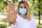 Woman in protective face mask showing stop gesture in park, focus on hand. Prevent spreading of coronavirus