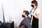 A woman in a protective mask on her face cuts hair to a man in a black mask on her face in a hairdressing salon