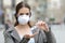 Woman with protective mask using hand sanitizer on street