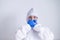 A woman in a protective suit and a mask covers her mouth with her hands in gloves on a white background. I do not speak