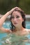 Woman pulling back her hair and glancing away from camera in the pool