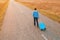 Woman pulling travel suitcase luggage on road in autumn sunset