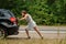 Woman pushing broken car on road, breakdown