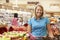 Woman Pushing Trolley By Fruit Counter In Supermarket