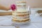 Woman puts flower rose on stylish naked cake. Cake decoration